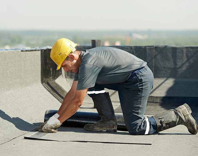 Construction worker kneeling and working on a rooftop.