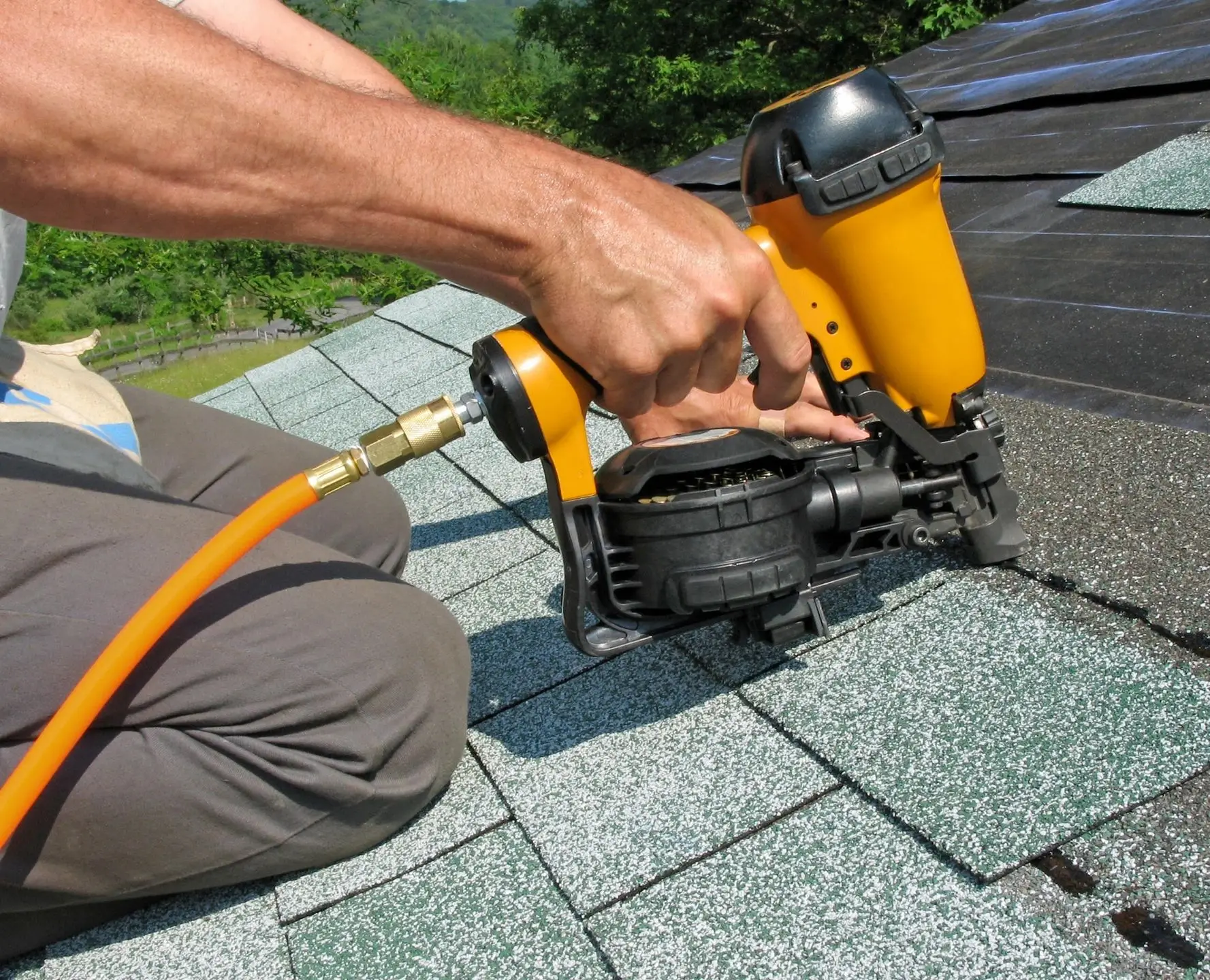 A person using a nail gun on roof shingles.