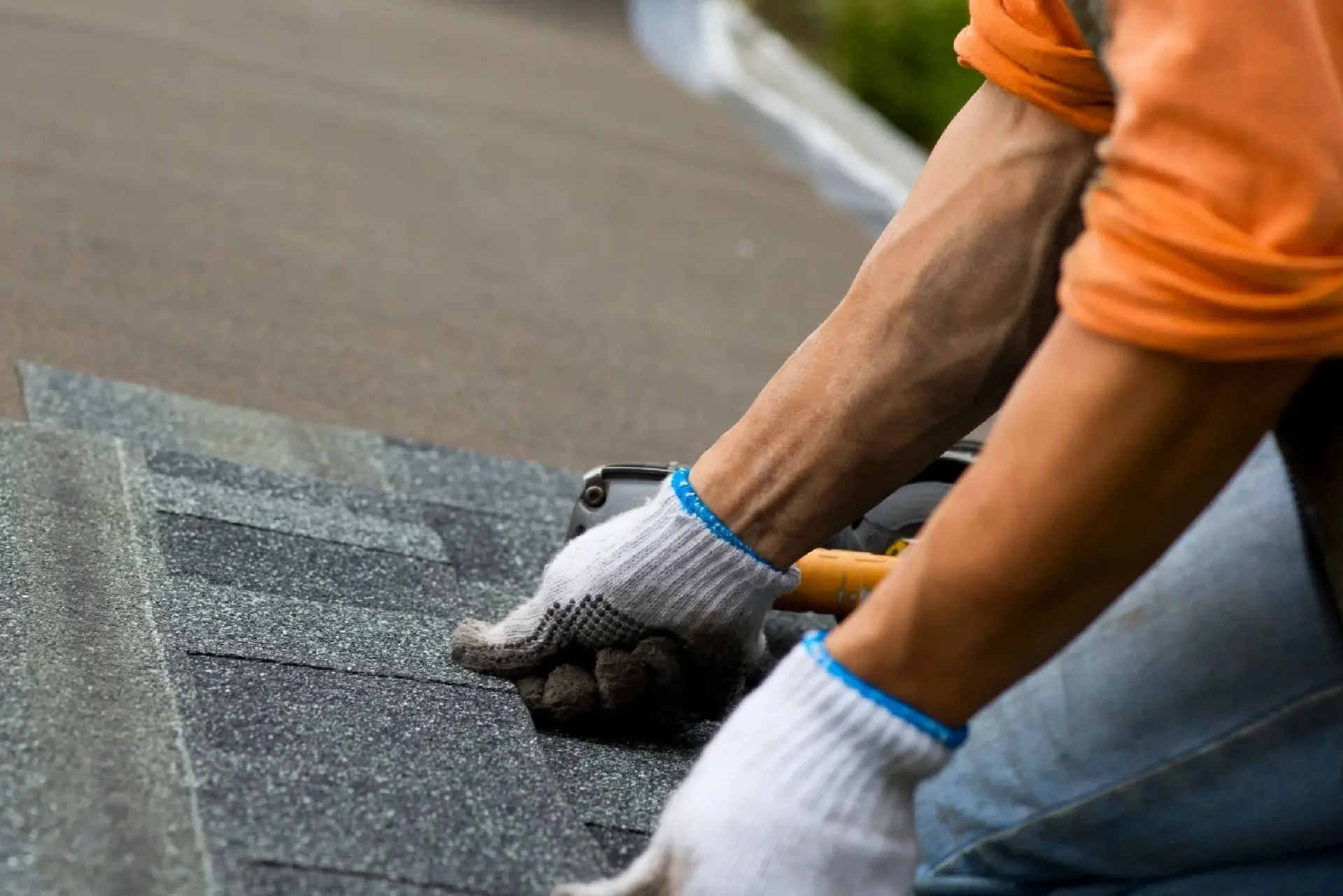 A person installing asphalt shingles on a roof wearing gloves.