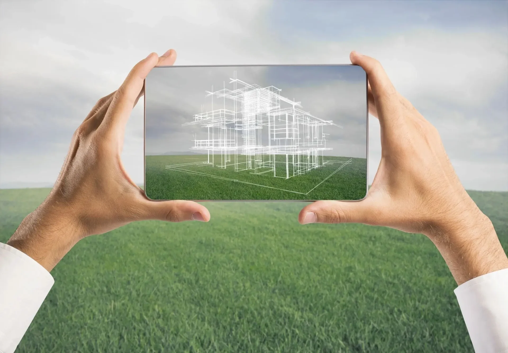 Hands holding a transparent screen with a house blueprint over a green field.